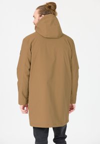 Bruine lange jas met capuchon, met een gladde textuur en rechte snit, gezien van achteren. Handen ontspannen langs de zijkanten.