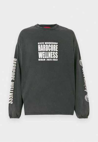 Tmavošedé tričko s dlhým rukávom a bielym textom "032C Workshop Hardcore Wellness Berlín 2025-2032" na prednej strane a rukávoch, s elastickými manžetami.