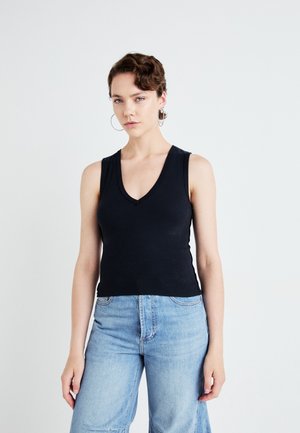 Zwarte mouwloze top met een V-hals ontwerp, gemaakt van ribbelstof. Gecombineerd met lichtblauwe wijde jeans. Eenvoudige, minimalistische stijl.
