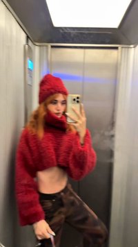 Pull court rouge et duveteux avec un col montant et des manches longues. Assorti à un pantalon foncé à motif camouflage. En arrière-plan, un ascenseur.