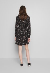 Black dress with long sleeves, floral pattern, cinched waist, and flared skirt. Worn with black footwear. Back view shown.