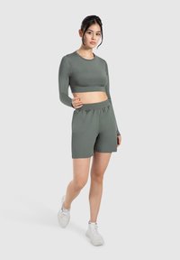 Träningsset i matt skoggrön, bestående av en kortärmad topp med lång ärm och högmidjade shorts, tillverkat av ett mjukt och elastiskt tyg.
