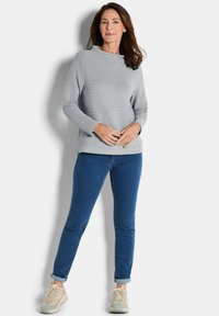 Lichtgrijze geribde trui met lange mouwen, ronde hals, gecombineerd met slim-fit blauwe denimjeans en beige sneakers. Eenvoudig en casual ontwerp.