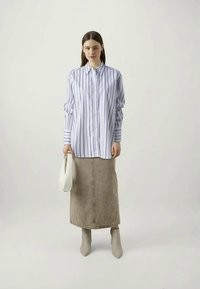 White button-up shirt with blue vertical stripes, paired with a beige denim long skirt and light gray ankle boots. Holding a white handbag.