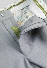 Grauener Stoff-Reißverschlusstasche mit einem Logo. Gefüttert mit einem gemusterten Stoff in Grüntönen und hellen Farben. Die Etiketten enthalten Pflegehinweise.