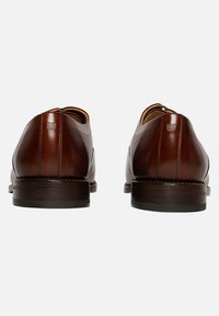 Chaussures en cuir brun avec une finition lisse, des accents texturés et une semelle basse, conçues avec un bout arrondi et un minimum de détails.