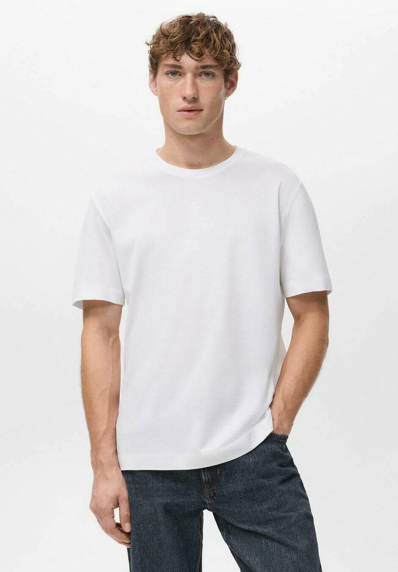 Biały t-shirt z krótkim rękawem i okrągłym dekoltem, o gładkiej fakturze i luźnym kroju, zestawiony z ciemnymi dżinsami.