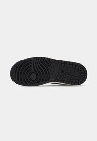 Sola de ténis Nike preta com padrões circulares e em grelha visíveis sobre um fundo branco simples.