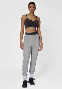 Szare spodnie dresowe wykonane z miękkiego materiału, w połączeniu z dopasowanym czarnym sportowym biustonoszem. Spodnie mają elastyczny pas i ściągacze przy kostkach.
