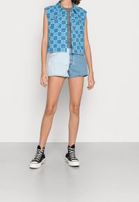 Gilet en denim avec un motif à carreaux bleu et bleu clair, doté de deux poches avant et d'une fermeture à boutons. Assorti à un short en denim bicolore.