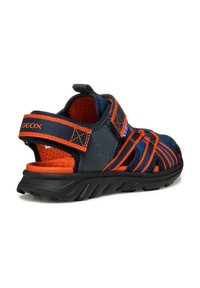 Sandelias en azul marino y naranja con correas de malla, cierres ajustables de gancho y bucle y una suela de goma negra texturizada. Perforaciones para transpirabilidad.