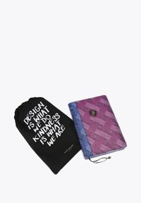 Cahier en tissu tissé violet et bleu avec une fermeture à bouton, à côté d'une pochette noire à cordon portant un texte blanc.