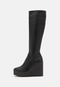 Black leather knee-high platform boots with a thick wedge heel, rounded toe, and smooth texture, featuring curved detailing on the side.