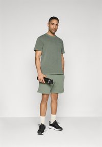 Olive green cotton t-shirt and matching shorts, featuring a relaxed fit. Black water bottle in hand, wearing black and white sneakers with cream socks.