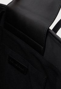 Κοντινό πλάνο ανοιχτής μαύρης τσάντας από δέρμα και ύφασμα που δείχνει μια εσωτερική τσέπη με μια μικρή μαύρη ετικέτα.