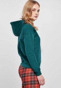 Bordeauxhuppari, jossa on kengurupussi, ribbatuet hihansuut ja nauhakuva, yhdistettynä punaisiin ja mustiin ruudullisiin slim-fit-housuihin.