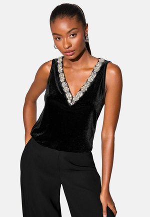 Black velvet sleeveless top with a deep V-neckline adorned with silver floral embroidery. Worn with black wide-leg pants.