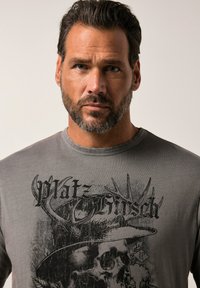 Šedé grafické tričko s černým designem lebky a parohů a textem "Platz Hirsch". Vyrobeno z hladké látky, zaoblený výstřih, krátké rukávy.