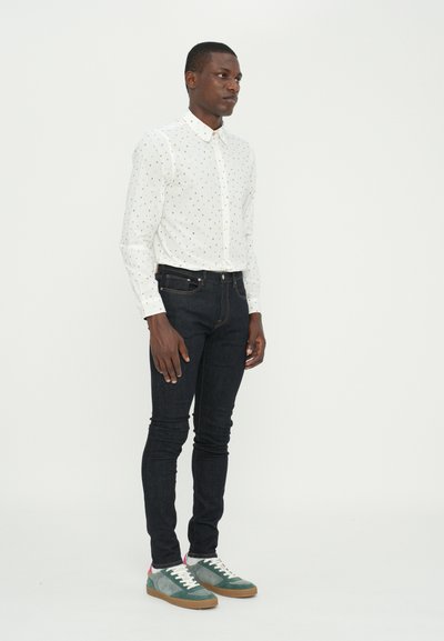 Chemise blanche à boutons avec des pois colorés, jean slim noir, et baskets multicolores avec une texture en suède et en toile.