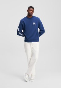 Maglione blu navy in cotone con collo rotondo, caratterizzato da una grafica bianca sul petto e "KARL LAGERFELD" stampato sulla manica.