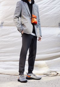 Grårandig kavaj över en svart hoodie, matchat med mörka sweatpants och grå sneakers. Inkluderar en orange axelväska för accenter.