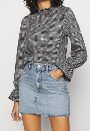 Blouse à manches longues à carreaux noir et blanc avec un col froncé, associée à une mini-jupe en denim bleu clair avec un ourlet effiloché et des poches avant.