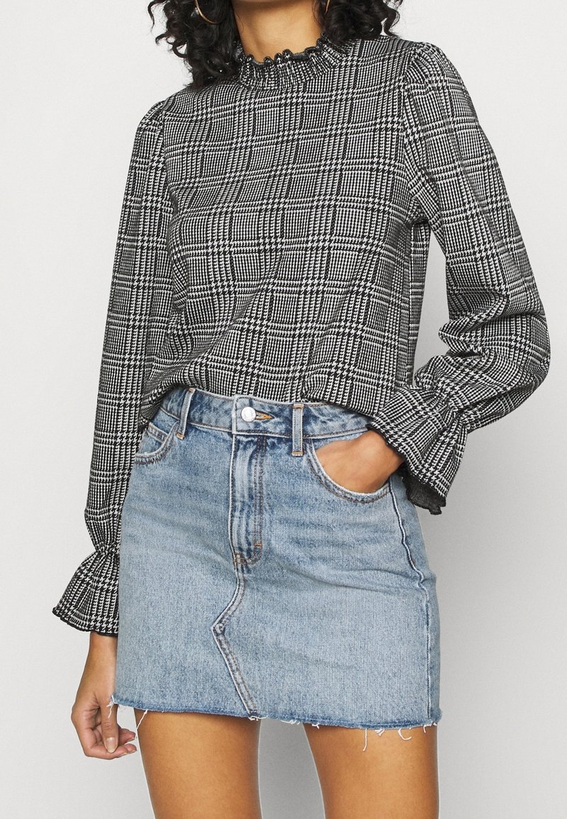 Blusa a maniche lunghe a scacchi bianca e nera con scollatura arricciata abbinata a una mini gonna in denim azzurro chiaro con orlo sfilacciato e tasche frontali.