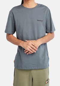 T-shirt gris à manches courtes en tissu de coton, avec un petit logo Timberland noir sur la poitrine gauche. Coupe classique avec un col rond.