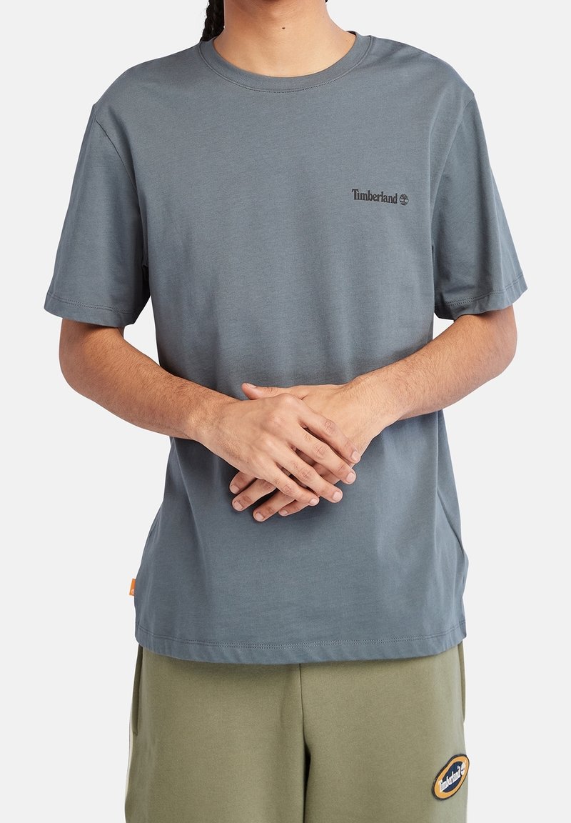 T-shirt gris à manches courtes en tissu de coton, avec un petit logo Timberland noir sur la poitrine gauche. Coupe classique avec un col rond.
