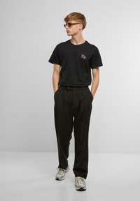 Black t-shirt with a small graphic, paired with high-waisted black trousers and grey sneakers. The outfit has a relaxed fit and minimal design.