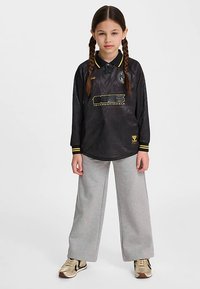 Schwarzes Langarm-Poloshirt mit strukturiertem Muster, gelbem Kragen und Akzenten, mit einem grafischen Logo. Kombiniert mit grauen, weit geschnittenen Hosen.