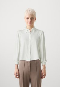 Kerge roheline pluus nööpide ja pehme voldiga õlgadel, pikkade puhvõistega, valmistatud siledast kangast. Eesmine äär on kergelt kaardus.