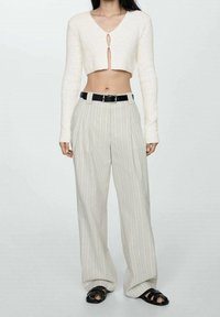 Valkoinen lyhyt neulepusero v-aukolla ja avausyksityiskohdalla, yhdistettynä suuriin, vaaleanharmaisiin pystyraidoitettuihin housuihin ja mustiin sandaaleihin.