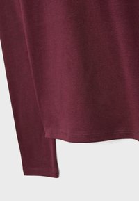 Burgundy long-sleeve top made from soft cotton, featuring a rounded hem, double-stitched seams, and a smooth texture.