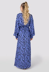 Robe longue bleue avec un motif à pois noir, taille élastique, manches longues et silhouette fluide, fabriquée en tissu léger.