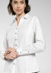 Witte blouse met een kraag, voorzien van metalen knopen en decoratieve stiksels langs de voorkant en de manchetten. Glad, geweven stof.
