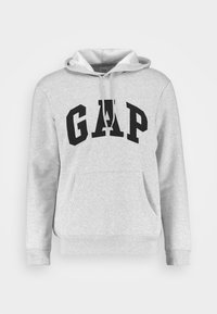 Felpa grigia chiara con il logo GAP nero sul petto, dotata di tasca frontale e cappuccio con lacci, su uno sfondo bianco.