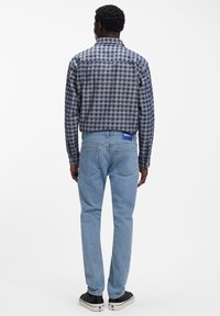 Ruuduline sinise ja halli tooniga pikkade varrukatega särk, millele on sobitatud helesinised teksad ja mustad tossud, millel on valged ja sinised detailid.