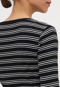 Black and white striped long-sleeve top with a ribbed texture, round neckline, and fitted design. Visible stitching detail.