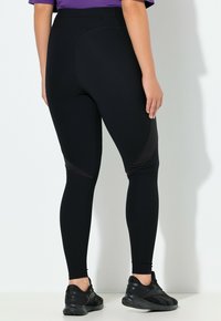 Czarne legginsy wykonane z teksturowanej tkaniny, z wysokim stanem i siateczkowymi wstawkami po bokach. Połączone z czarnymi butami sportowymi.