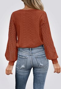 Roestkleurige kant bovenkant met ballonnenmouwen en een ruitpatroon; gecombineerd met hoog-waist blauwe versleten jeans, die een getailleerde silhouet laten zien.
