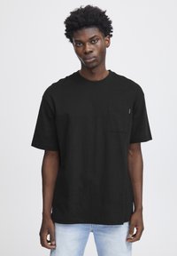 Tricou din bumbac negru cu decolteu rotund, mâneci scurte și buzunar pe piept. Materialul are o textură netedă și o croială lejeră.