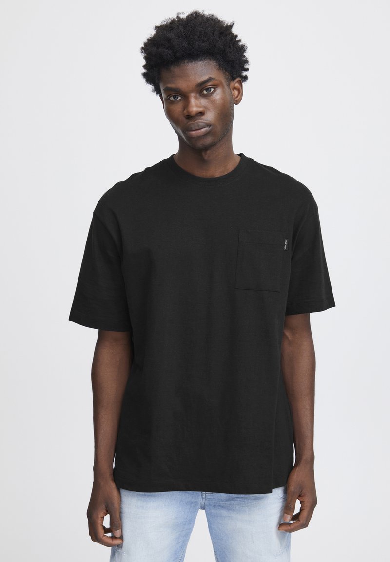 Tricou din bumbac negru cu decolteu rotund, mâneci scurte și buzunar pe piept. Materialul are o textură netedă și o croială lejeră.