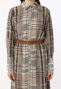 Button-up shirt dress in a plaid pattern featuring earthy tones, long sleeves, and a brown belt with a square gold buckle.