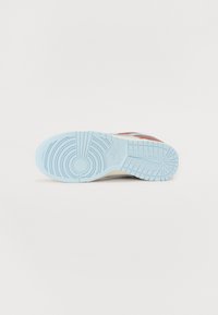 Sapatilha Nike com uma sola de borracha azul, padrão de piso texturizado e uma combinação de materiais em vermelho, branco e bege na parte superior.