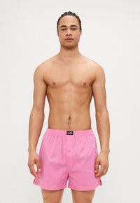 Ανοιχτό ροζ μαγιό με ελαστική μέση και μια μικρή λεπτομέρεια κουμπιού. Το ύφασμα είναι λείο και ελαφρύ, κατάλληλο για θαλάσσιες δραστηριότητες.