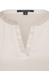 Satin-bluse in hellbeige mit V-Ausschnitt und einem dezenten Glanz. Das Etikett trägt die Aufschrift "comma, 36" auf einem schwarzen Label. Glatte Textur, minimales Design.