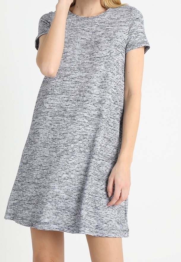Femme portant une robe décontractée à manches courtes, grise avec de fines rayures noires, debout devant un fond uni.