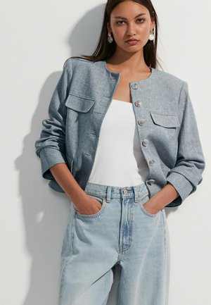 Light blue denim jacket with long sleeves, button closure, and two front pockets, paired with a white top and light blue jeans.