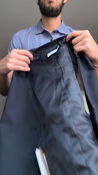 Homme en chemise bleue tenant ouverte une veste noire, montrant la doublure intérieure et une étiquette blanche à l’intérieur.